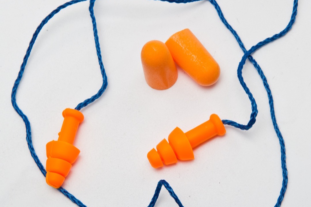 Orange foam ear plugs and orange triple-flange reusable corded ear plugs on a white background, the two plug styles travellers most often compare for flying