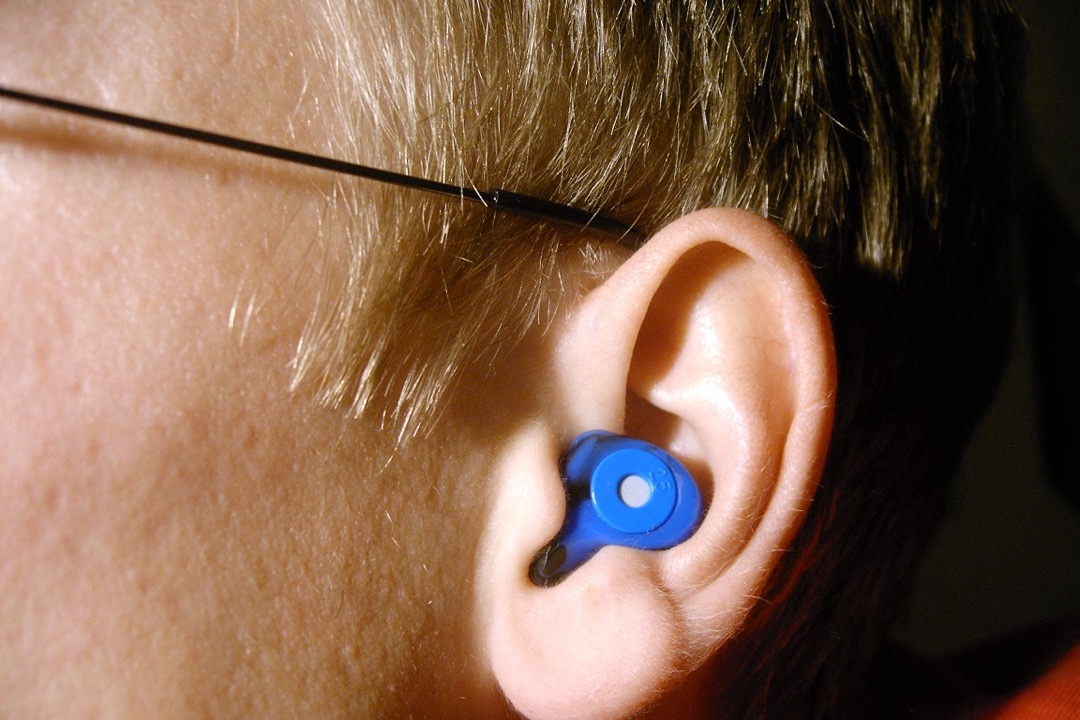 A blue filtered earplug seated in the outer ear, showing the low-profile fit concert ear plugs use to lower volume without muffling music