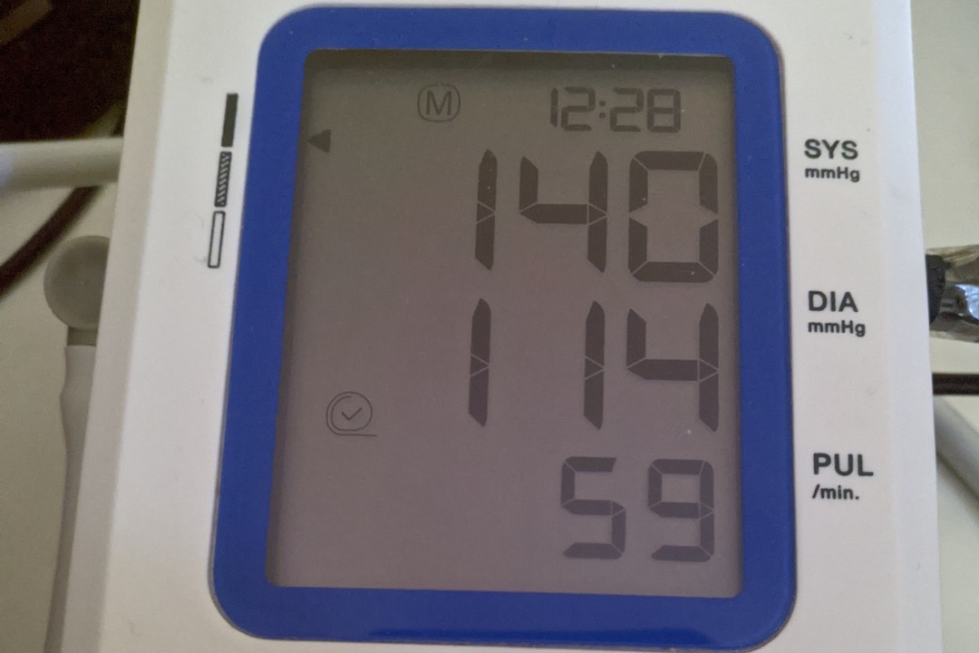 Automatic upper-arm blood pressure monitor displaying a systolic over diastolic reading with the AHA category chart in the background