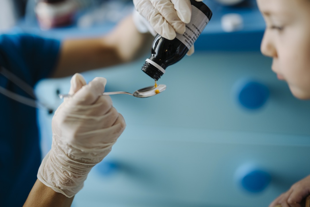 A caregiver measuring a dose of children's cough medicine onto a spoon at home