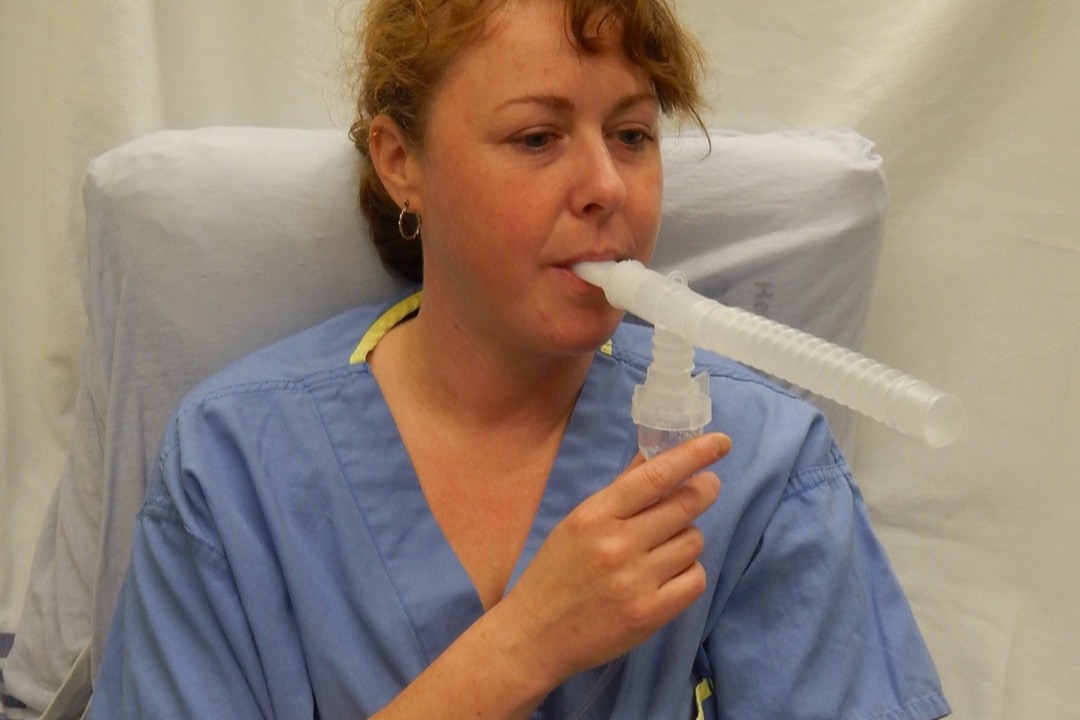 A patient using a nebulizer with the medication cup, mouthpiece, and tubing visible — the reusable parts that require cleaning after every treatment
