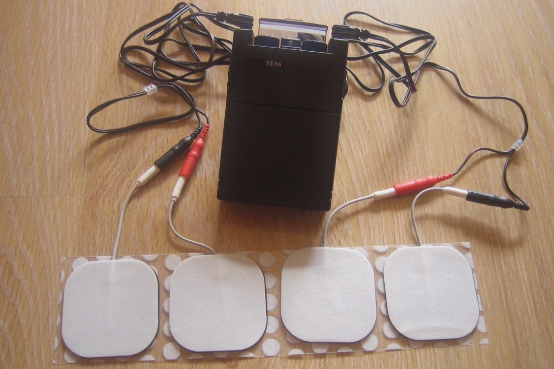 A handheld TENS unit with two lead wires connected to a pair of self-adhesive electrode pads placed on a person's lower back