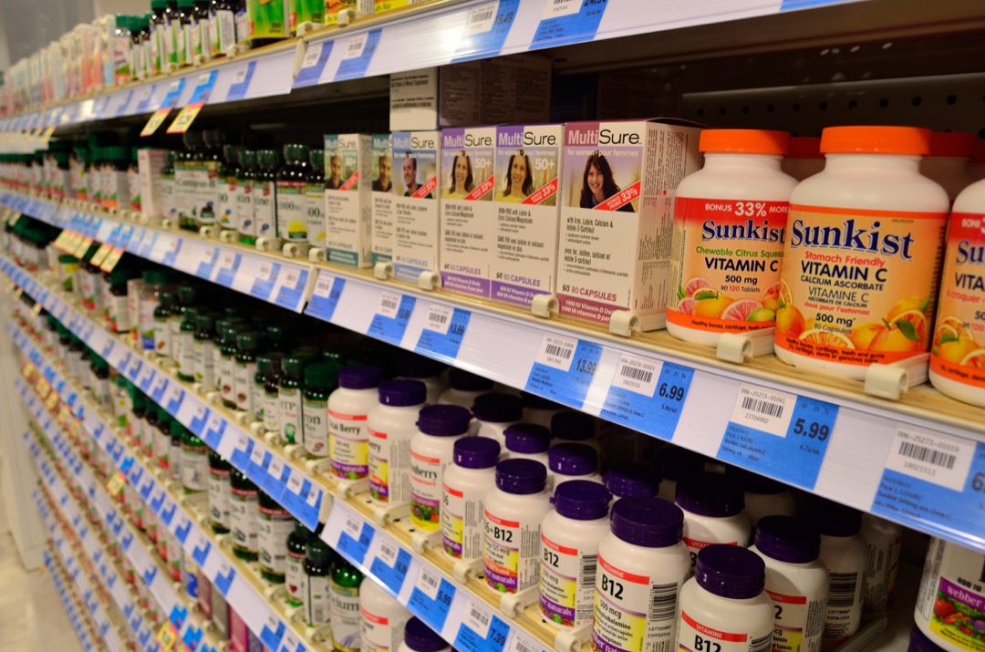 Pharmacy shelf stocked with vitamin C, B12 and multivitamin supplement bottles